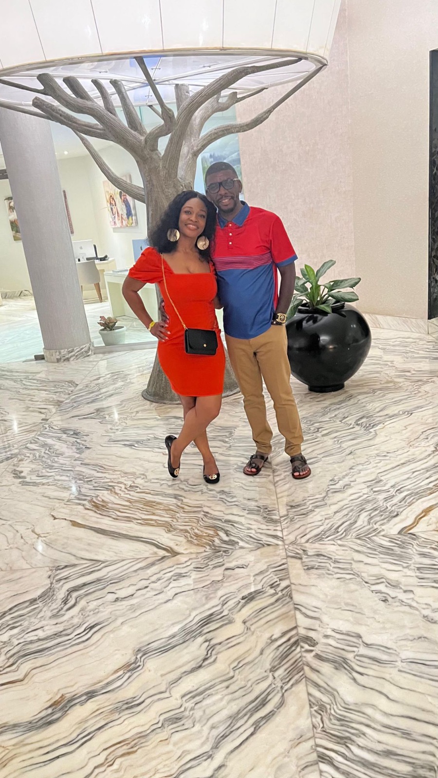 The couple in a marble hotel lobby, Sylvia in a red dress